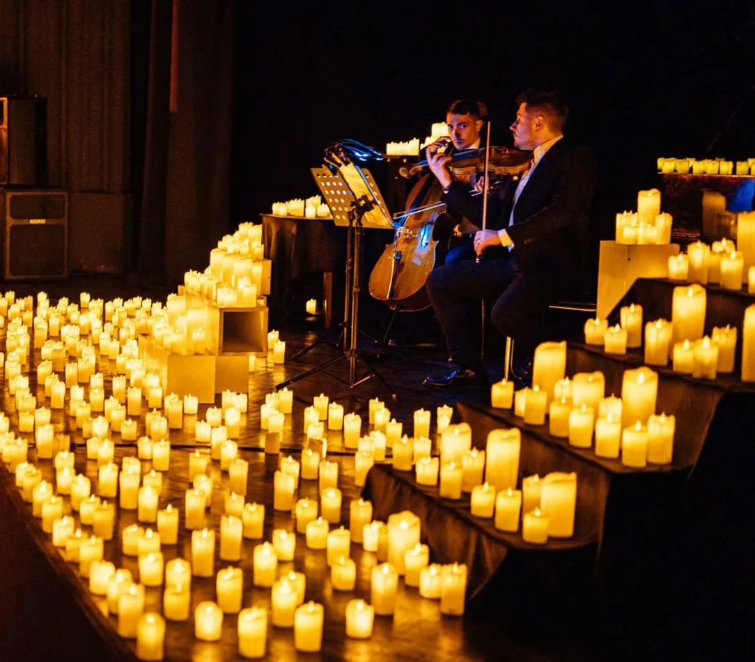 A candlelit theater with a string ensemble performing holiday music.