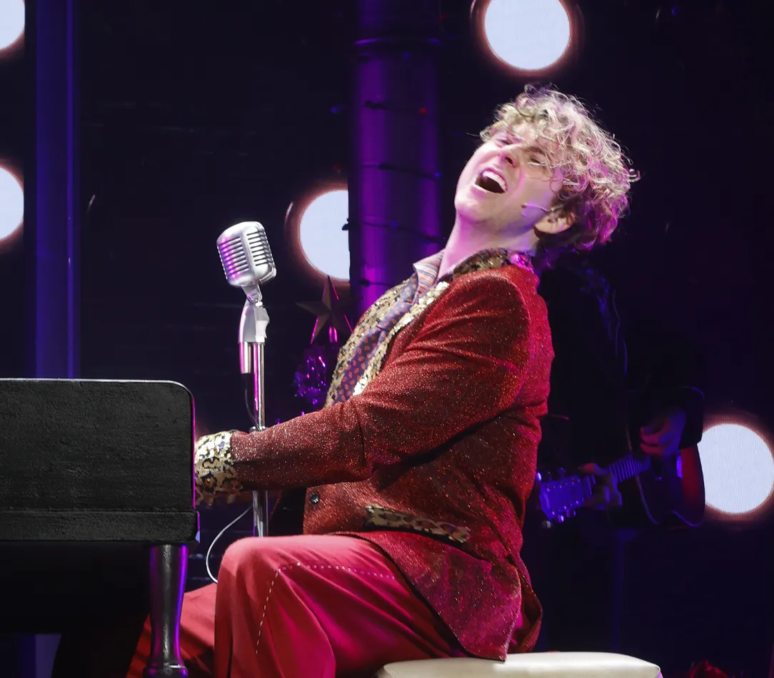 Sean McGibbon performing on stage with a piano and energetic lighting.